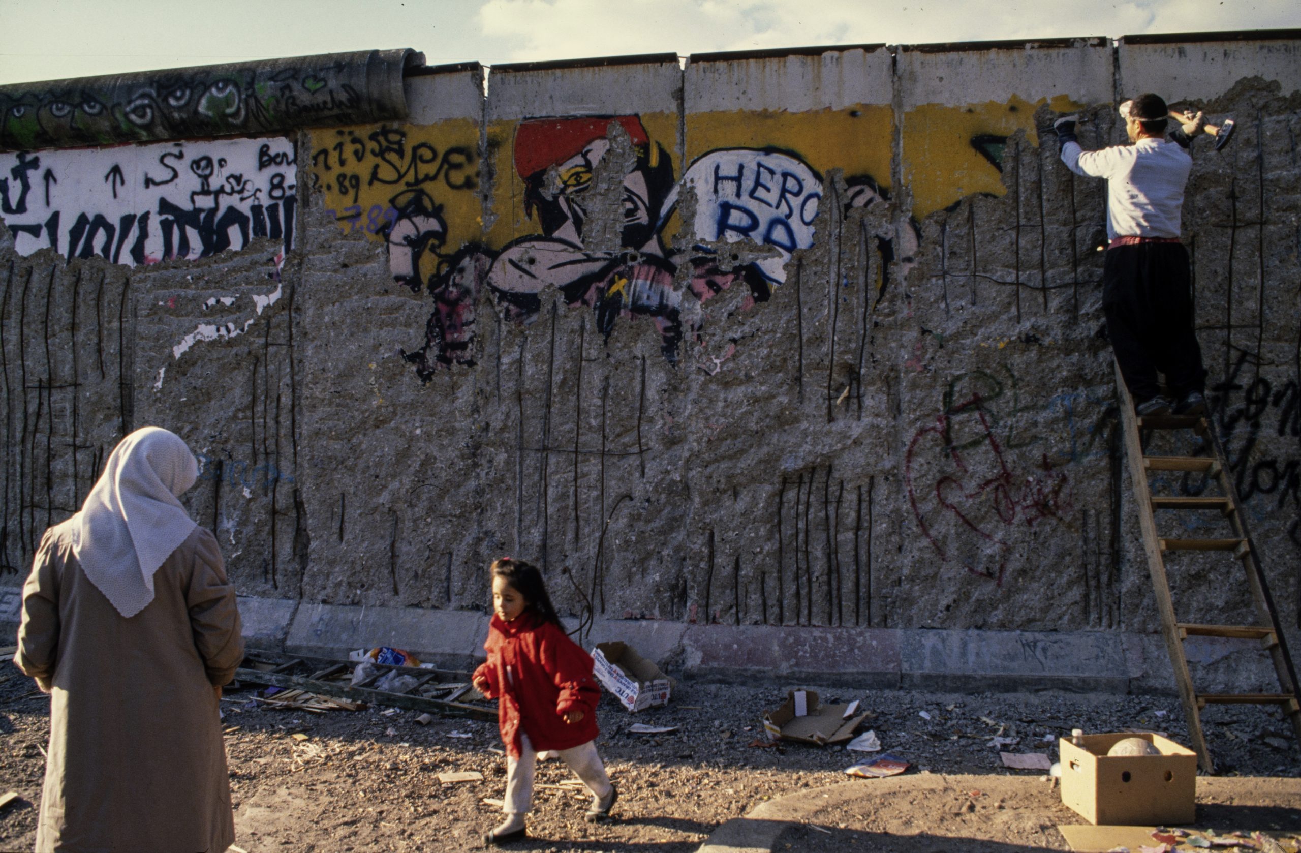 Die Mauer steht für die deutsche Teilung und den Kalten Krieg. Menschen schlugen Mauerteile als Erinnerung aus der Mauer. Diese Menschen heißen "Mauerspechte". Sie haben die Mauerstücke behalten oder verkauft. Foto um 1990.